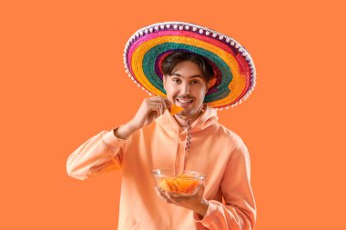 Turuncu arka planda cipsleri olan genç Meksikalı adam.