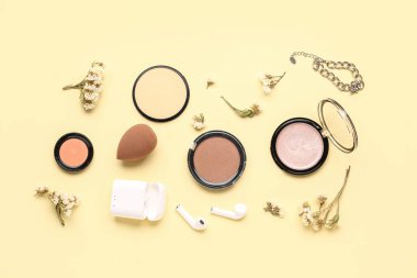Makyaj ürünleriyle kompozisyon. modern kulaklıklar ve güzel çigila çiçekleri bej arka planda
