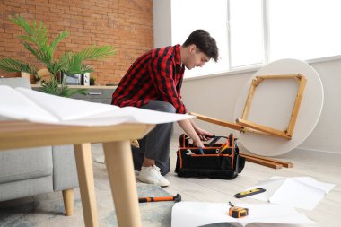 Bir çanta alet edevat taşıyan erkek işçi mutfakta mobilya monte ediyor.