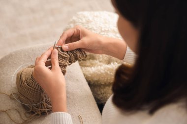 Evde iğnelerle örgü ören genç bir kadın, yakın plan.