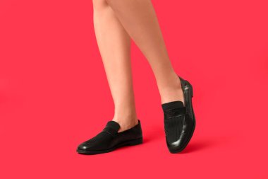 Kırmızı arka planda siyah ayakkabılı genç bir kadının bacakları.