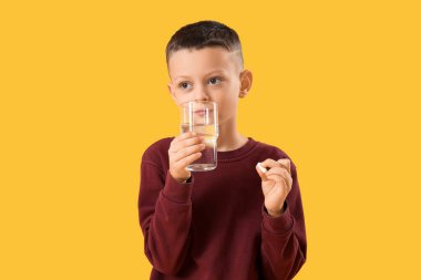 Sarı arka planda bir bardak su ve hap olan hasta küçük çocuk.