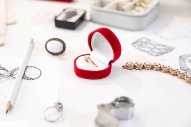 Atölyedeki kuyumcu masasında üzerinde alet ve nişan yüzüğü olan şık aksesuarların çizimleri.