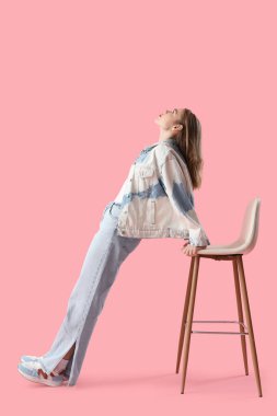 Pembe arka planda dışkısı olan açık mavi kotlu genç bir kadın.