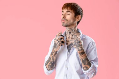 Dövmeli genç adam pembe arka plana parfüm sürüyor.