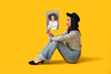 Şık kotlu, dergisi sarı arka planda oturan güzel Asyalı kadın.