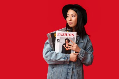 Kırmızı arka planda dergisi olan şık kot ceketli güzel bir Asyalı kadın.