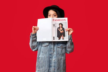 Kırmızı arka planda dergisi olan şık kot ceketli güzel bir Asyalı kadın.