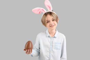 Gri arka planda çikolata yumurtası olan tavşan kulaklı mutlu bir çocuk. Paskalya kutlaması