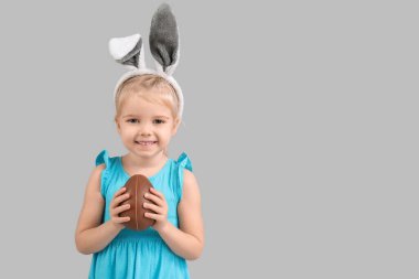 Gri arka planda çikolata yumurtası olan tavşan kulaklı mutlu küçük kız. Paskalya kutlaması