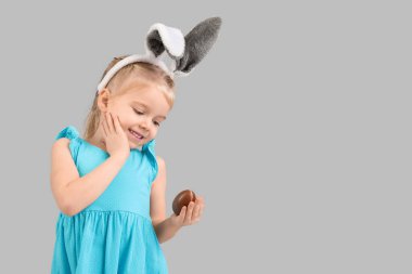 Gri arka planda çikolata yumurtası olan tavşan kulaklı mutlu küçük kız. Paskalya kutlaması