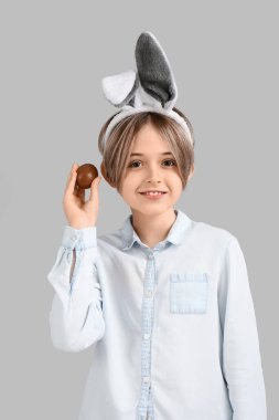 Gri arka planda çikolata yumurtası olan tavşan kulaklı şirin bir çocuk. Paskalya kutlaması