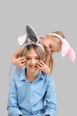 Gri arka planda çikolata yumurtası olan tavşan kulaklı şirin çocuklar. Paskalya kutlaması