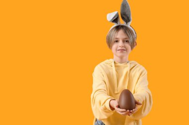 Sarı arka planda çikolata yumurtası olan tavşan kulaklı şirin bir çocuk. Paskalya kutlaması