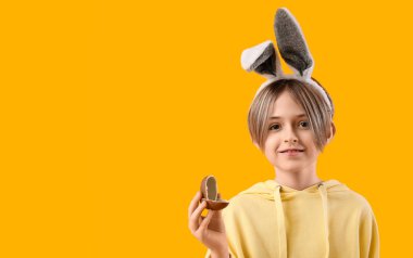 Sarı arka planda yarım çikolatalı yumurtası olan tavşan kulaklı şirin bir çocuk. Paskalya kutlaması