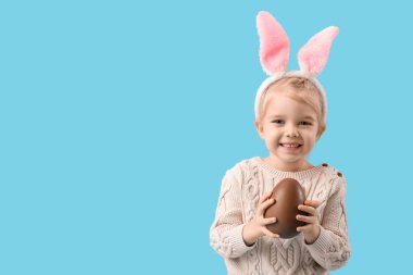 Mavi arka planda çikolata yumurtası olan tavşan kulaklı mutlu küçük kız. Paskalya kutlaması