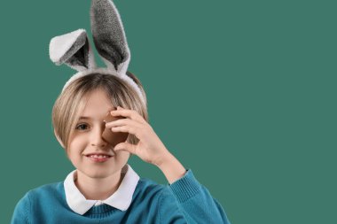 Yeşil arka planda çikolatalı yumurtası olan tavşan kulaklı şirin bir çocuk. Paskalya kutlaması