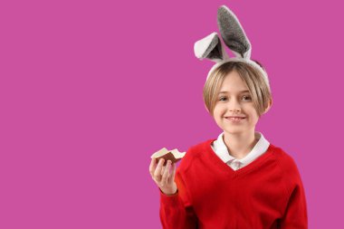 Tavşan kulaklı şirin çocuk mor arka planda çikolata yumurtası yiyor. Paskalya kutlaması