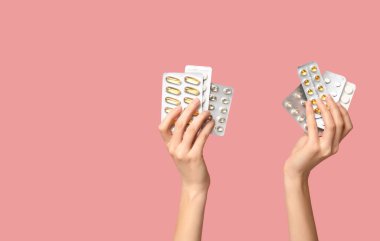 Kadın eli, pembe arka planda su toplayan paketlerde hapları tutuyor.