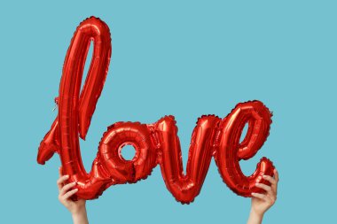 Mavi arka planda aşk kelimesi şeklinde balonu olan bir kadın. Sevgililer Günü kutlaması