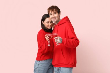 Pembe arka planda şarap bardakları olan genç bir çift. Sevgililer Günü kutlaması