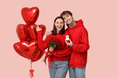 Nişan yüzüklü genç bir çift, kalp şeklinde hava balonları ve pembe arka planda bir buket gül. Sevgililer Günü kutlaması