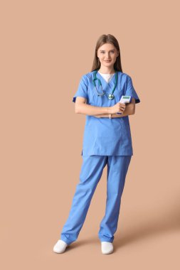 Bej arka planda kızılötesi termometresi olan güzel bir doktor.