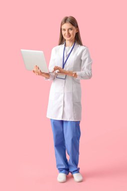Güzel doktor pembe arka planda dizüstü bilgisayar kullanıyor.