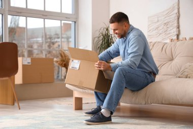 Evdeki kanepede paketleri açan genç adam.