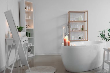 İçinde yanan mumlar, küvet ve ayna olan hafif bir banyo.