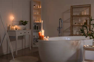 İçinde yanan mumlar, küvet ve masa olan karanlık bir banyo.