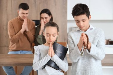 İncil 'i ve boncukları olan küçük çocuklar mutfakta dua ediyorlar.