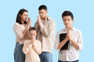 İncil 'i olan küçük bir çocuk ve ailesi mavi arka planda dua ediyor.