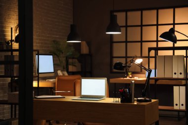 Karanlık ofis, iş yeri, boş laptop ve geceleri parlayan lambalar.