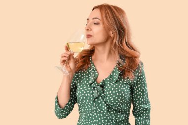 Bej arka planda bir bardak şarabı olan güzel olgun bir kadın.