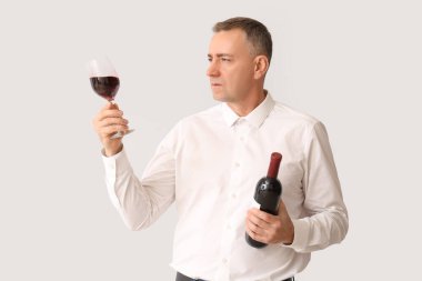 Beyaz arka planda cam ve şarap şişesi olan yakışıklı olgun bir adam.