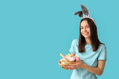 Tavşan kulaklı ve mavi arka planda Paskalya sepeti olan güzel bir genç kadın.