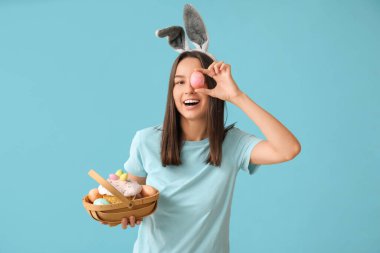 Tavşan kulaklı ve mavi arka planda Paskalya sepeti olan güzel bir genç kadın.