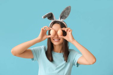 Mavi arka planda tavşan kulaklı ve Paskalya yumurtalı komik genç kadın.