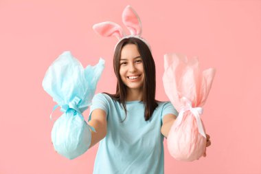 Tavşan kulaklı güzel bir bayan ve pembe arka planda Paskalya hediyeleri.