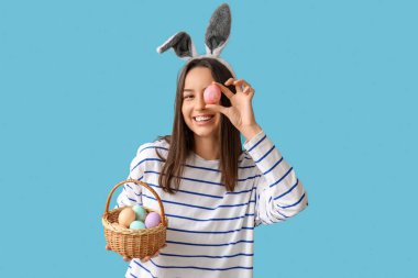 Tavşan kulaklı ve mavi arka planda Paskalya sepeti olan güzel bir genç kadın.
