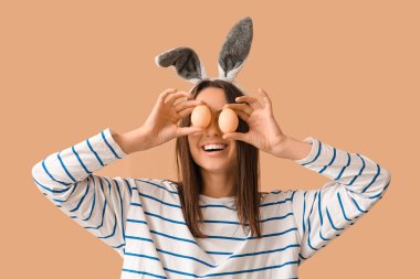 Tavşan kulaklı ve bej arka planda Paskalya yumurtası olan komik genç bir kadın.