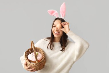 Tavşan kulaklı ve gri arka planda Paskalya sepeti olan güzel bir genç kadın.