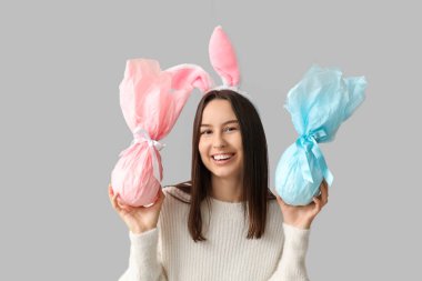 Tavşan kulaklı ve gri arka planda Paskalya hediyeli güzel bir genç kadın.