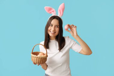 Tavşan kulaklı ve mavi arka planda Paskalya yumurtası sepeti olan güzel bir genç kadın.
