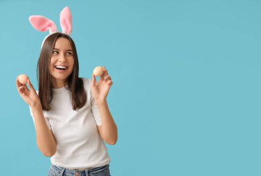 Tavşan kulaklı ve mavi arka planda Paskalya yumurtaları olan güzel genç bir kadın.