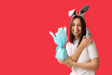 Tavşan kulaklı güzel bir genç kadın, oyuncak tavşan ve kırmızı arka planda Paskalya hediyesi.