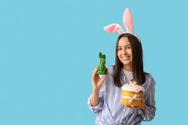 Tavşan kulaklı güzel bir genç kadın, oyuncak tavşan ve mavi arka planda Paskalya pastası.