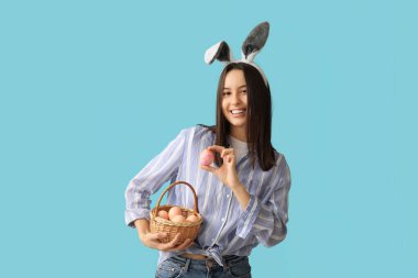 Tavşan kulaklı ve mavi arka planda Paskalya yumurtası sepeti olan güzel bir genç kadın.