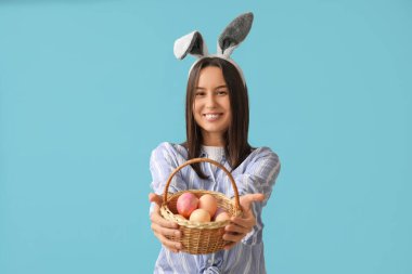 Tavşan kulaklı ve mavi arka planda Paskalya yumurtası sepeti olan güzel bir genç kadın.